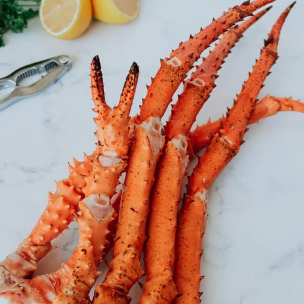 Bright orange crab legs with a cracker and lemon wedges on a white marble surface.
