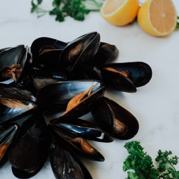 A pile of fresh mussels with parsley and lemon halves on a white surface.
