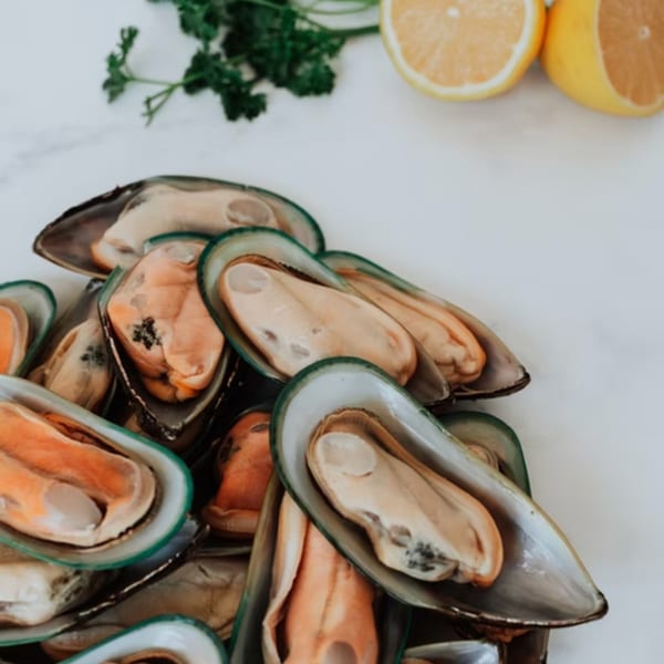 Fresh mussels with parsley and lemon halves on a white marble surface at Crackin' Crab.