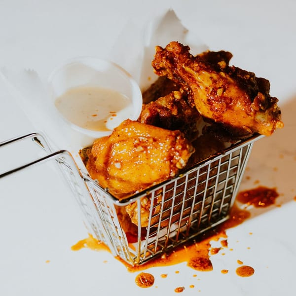 Crispy, saucy chicken wings in a metal basket with a side of dipping sauce.