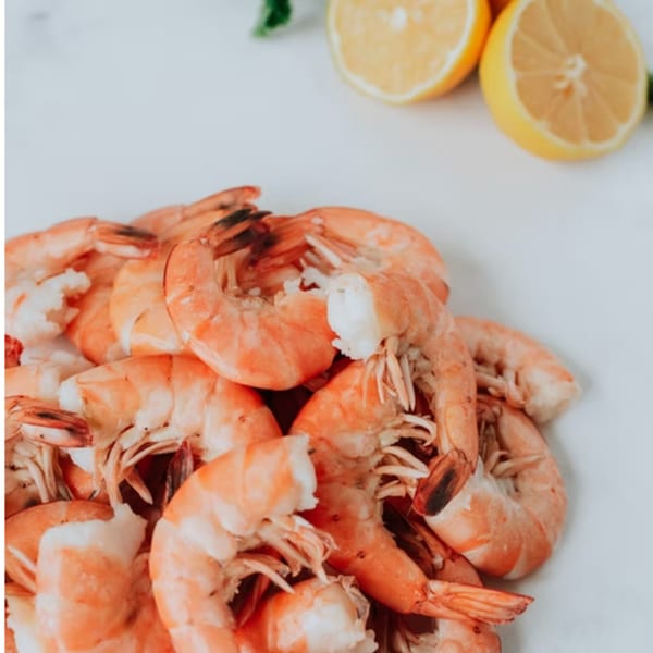 A pile of cooked shrimp with two lemon halves and a green herb in the background.