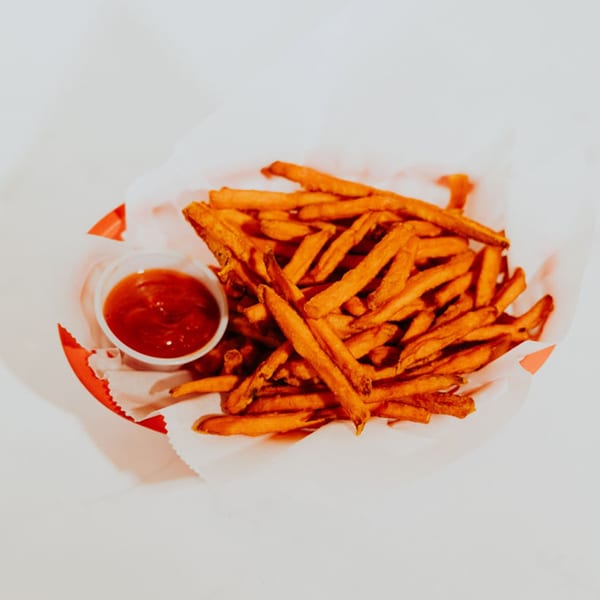 A red basket filled with crispy sweet potato fries and a small cup of ketchup.