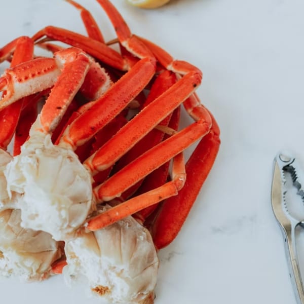 Bright red crab legs and white crab meat with a cracker and lemon wedge on a white surface.