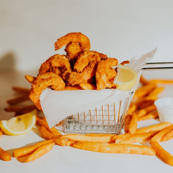 Crispy fried shrimp in a metal basket with a lemon wedge, surrounded by french fries.