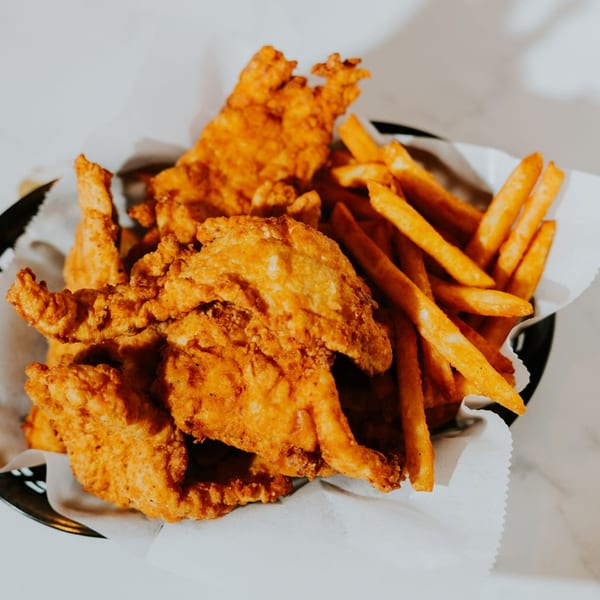 Crispy fried chicken tenders and golden french fries served in a basket lined with white paper.